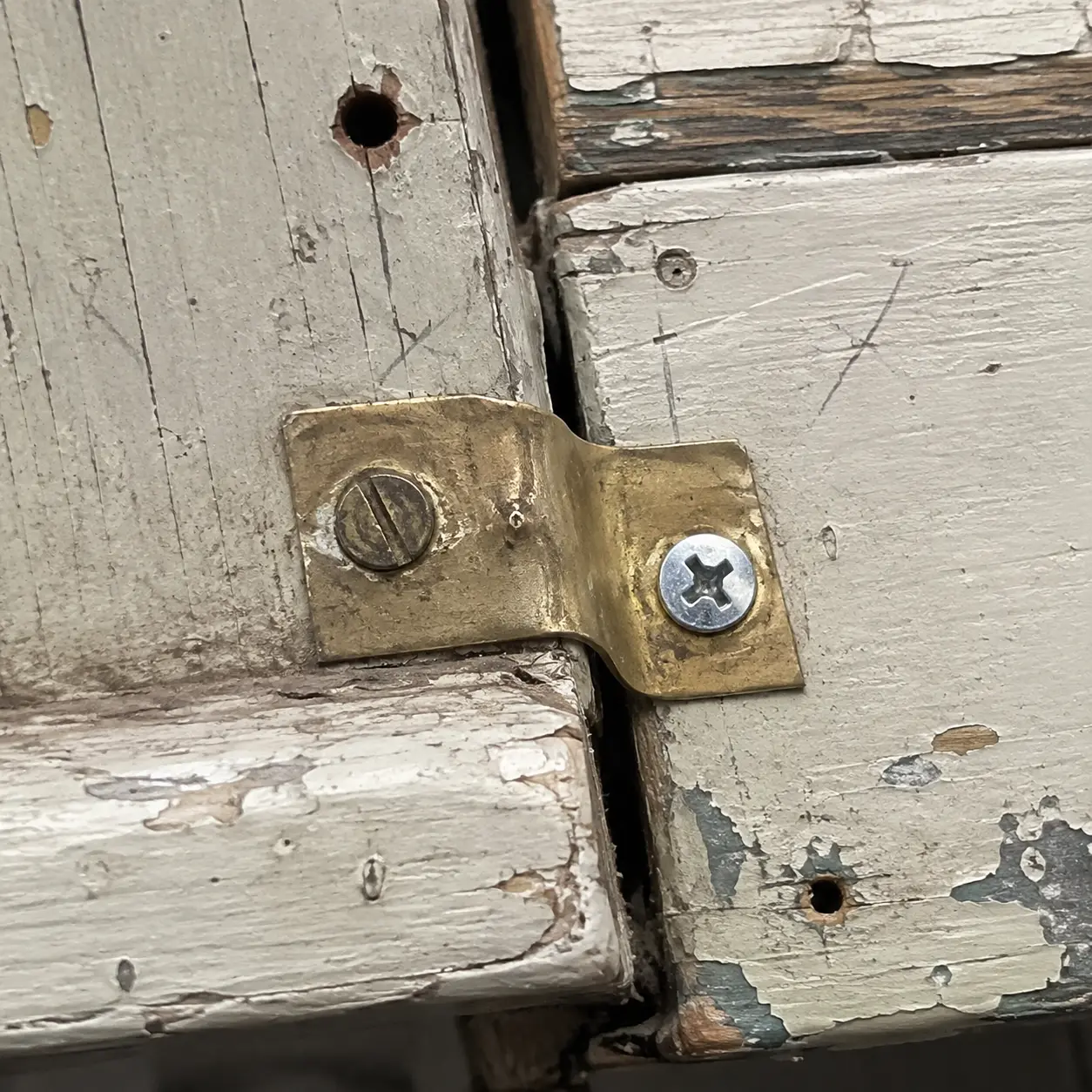 A folded brass repair plate joining worn painted timber with two different screws